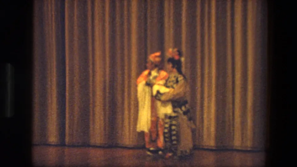 Two adult performers in ornate stage costumes move close together during the 1974 India dance performance.