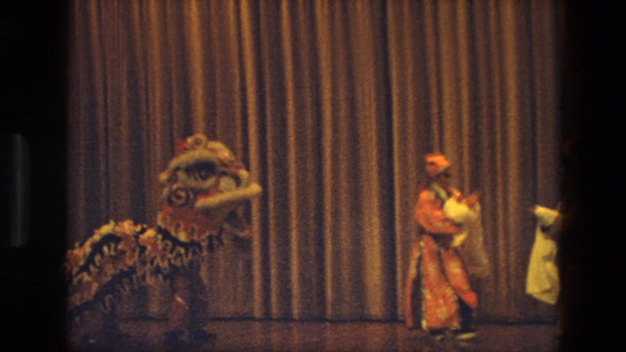 1974 India stage scene with a lion dance costume and a performer in red-orange clothing holding pale fabric.