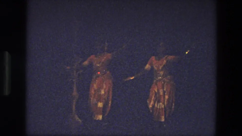 1974 India 8mm frame showing two costumed dancers on a darker stage, partly obscured by low exposure and grain.