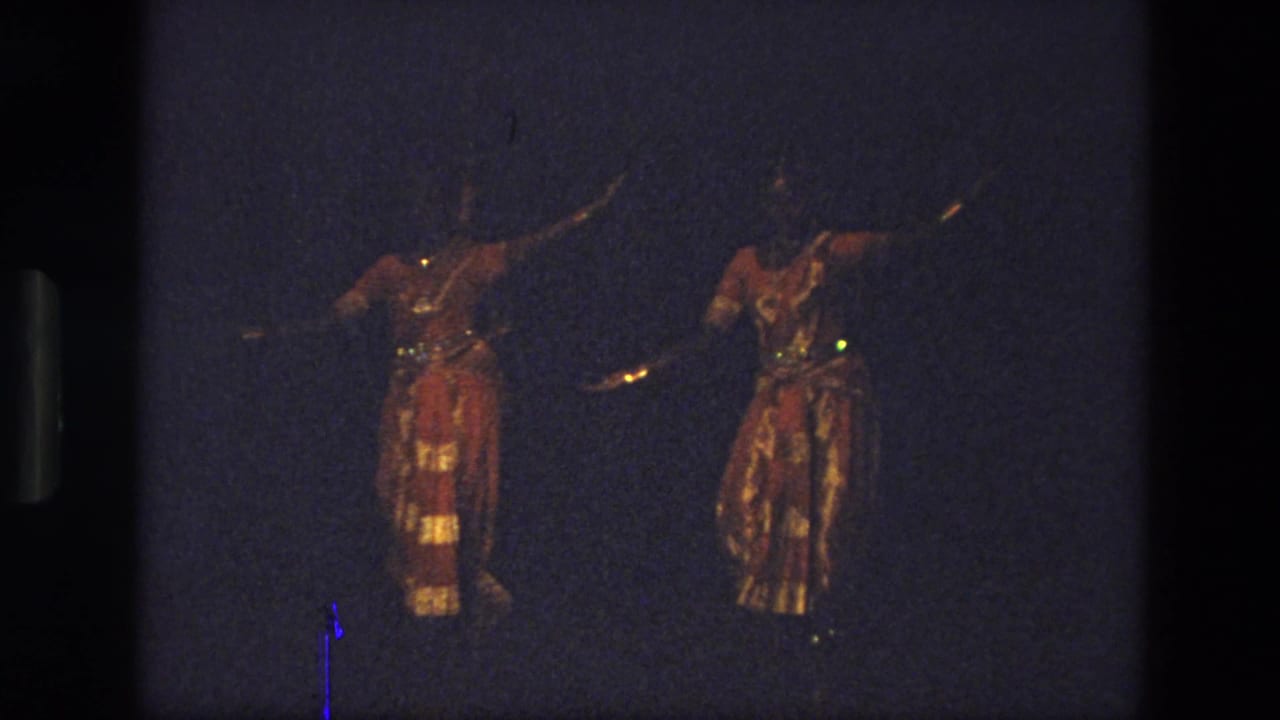 Two red-and-gold costumed dancers continue a synchronized pose on a dark stage.
