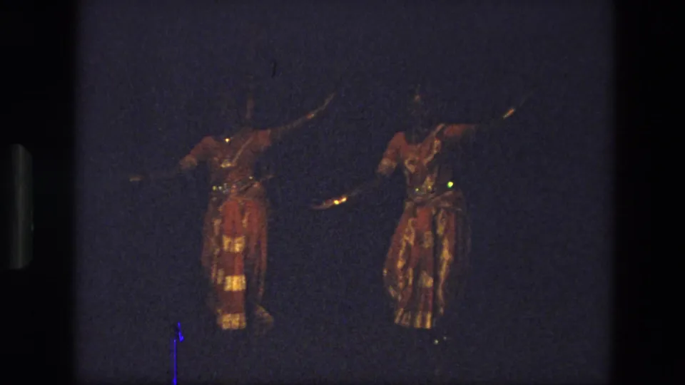 The 1974 India frame shows two performers in shimmering red-and-gold attire moving in parallel against a blue-black stage background.