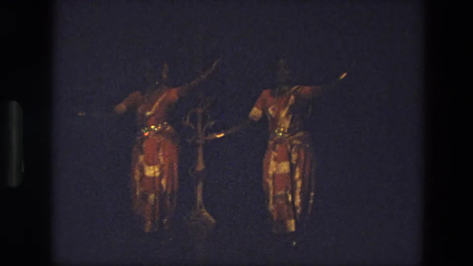 Two women in red-and-gold stage costumes appear mid-performance, with a darker central shape or possible performer partly visible between them.