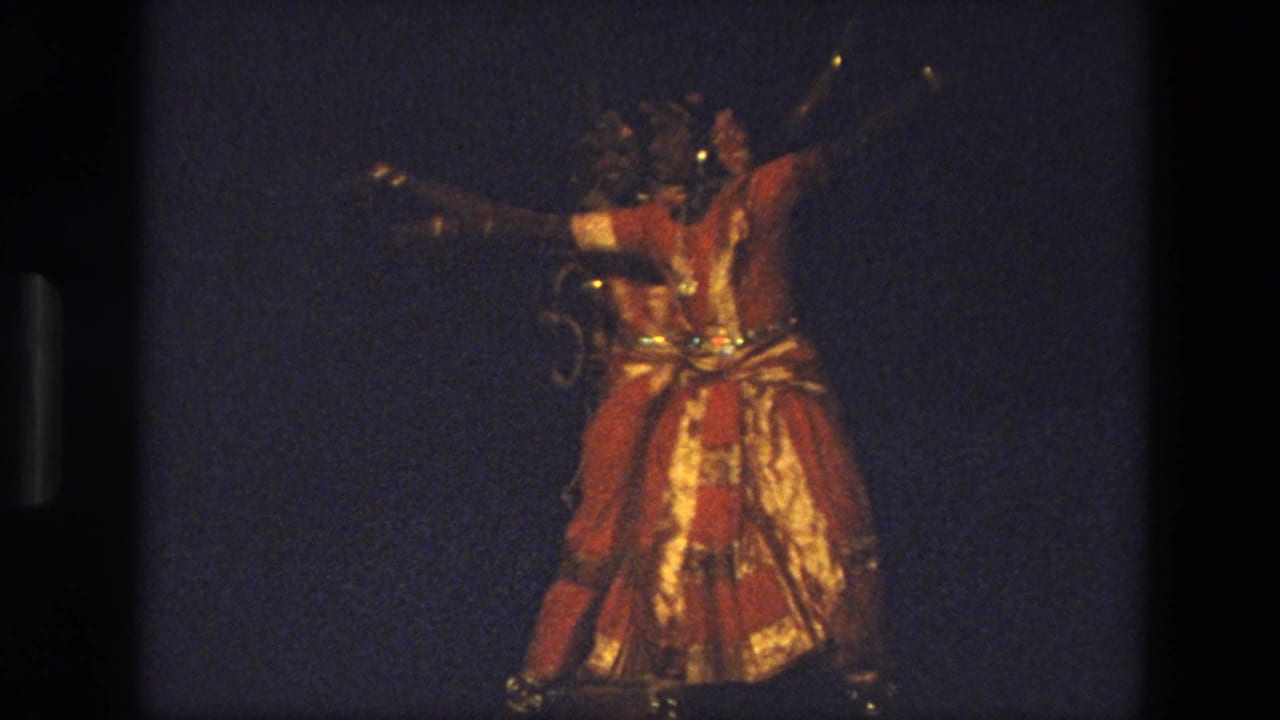 Dancer in red and gold costume performs on a dimly lit stage.