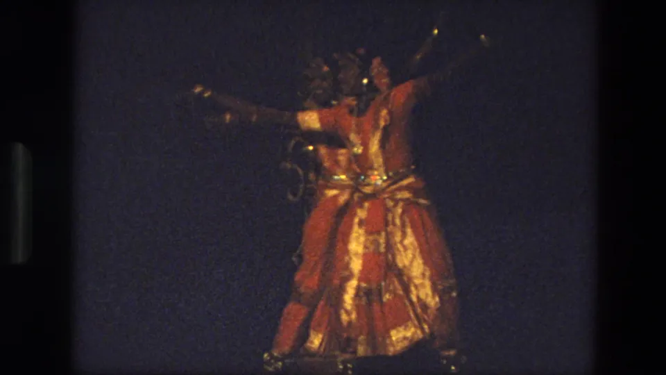 1974 India 8mm frame showing a dancer in a red and gold traditional-looking costume on a dark stage, with film borders visible.