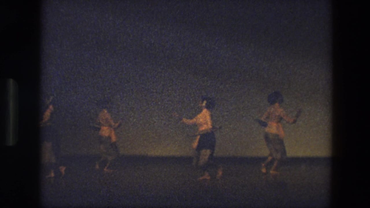 1974 India 8mm frame showing three dancers in motion on a dark stage, captured from an audience perspective with heavy grain.
