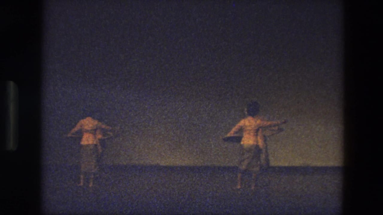 1974 India 8mm frame showing two dancers from behind on a dim stage, with warm exposure and visible film grain.