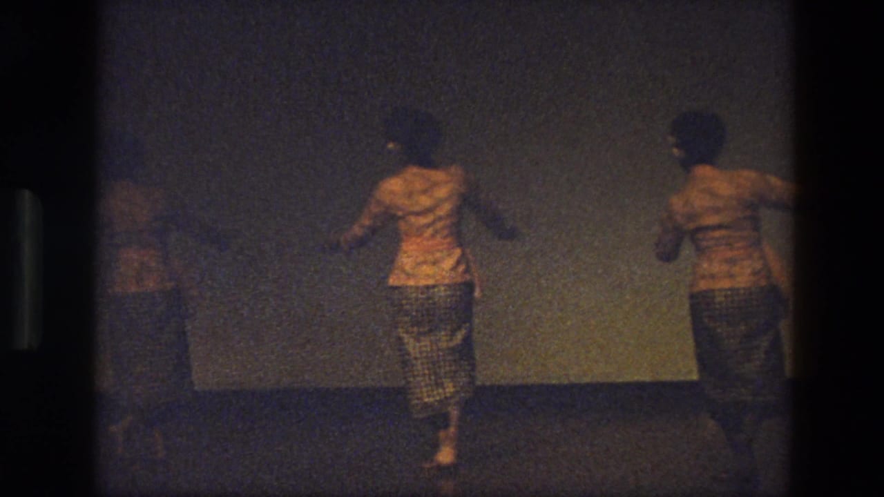 Women in yellow costumes dance on a stage, partly framed by dark film borders.