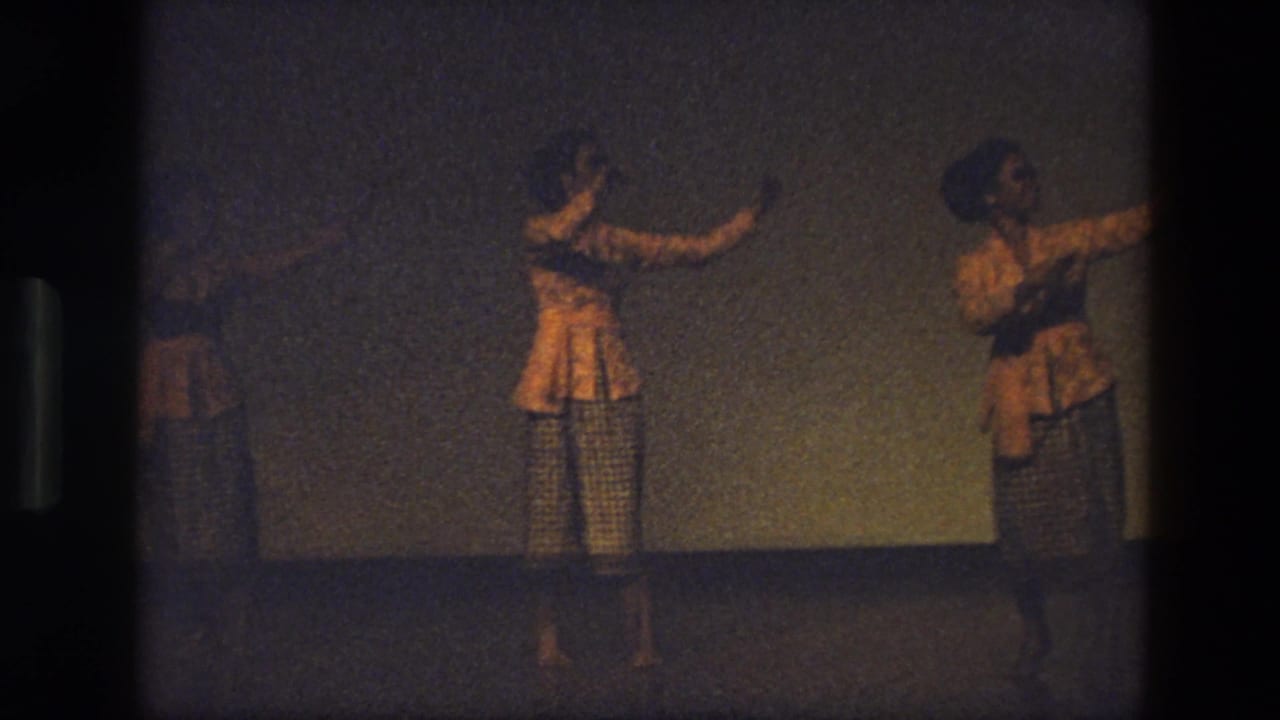 1974 India 8mm frame with women in matching yellow and checkered costumes moving in formation on stage.