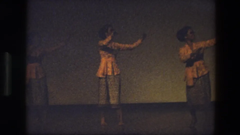 1974 India 8mm frame with women in matching yellow and checkered costumes moving in formation on stage.