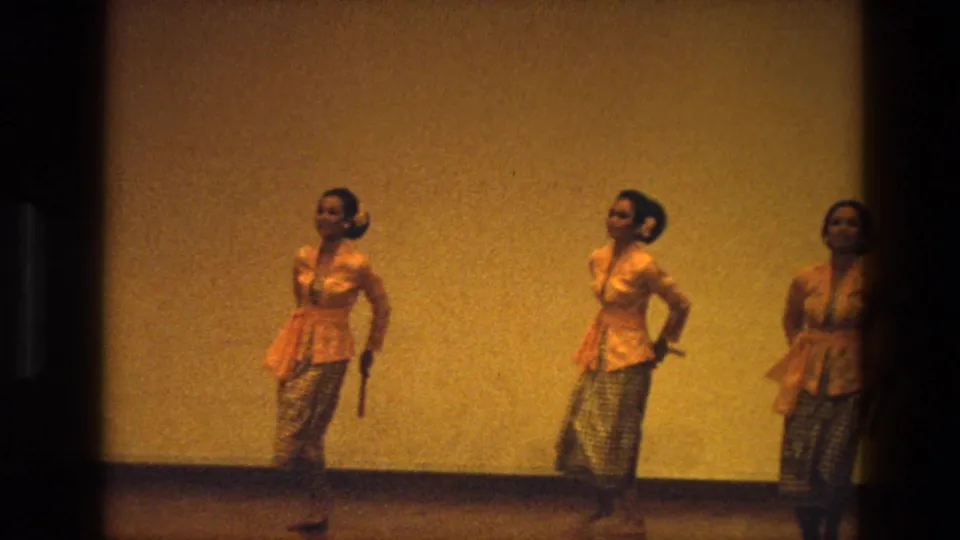 1974 India 8mm frame showing three women in yellow stage outfits holding sticks during a dance performance.