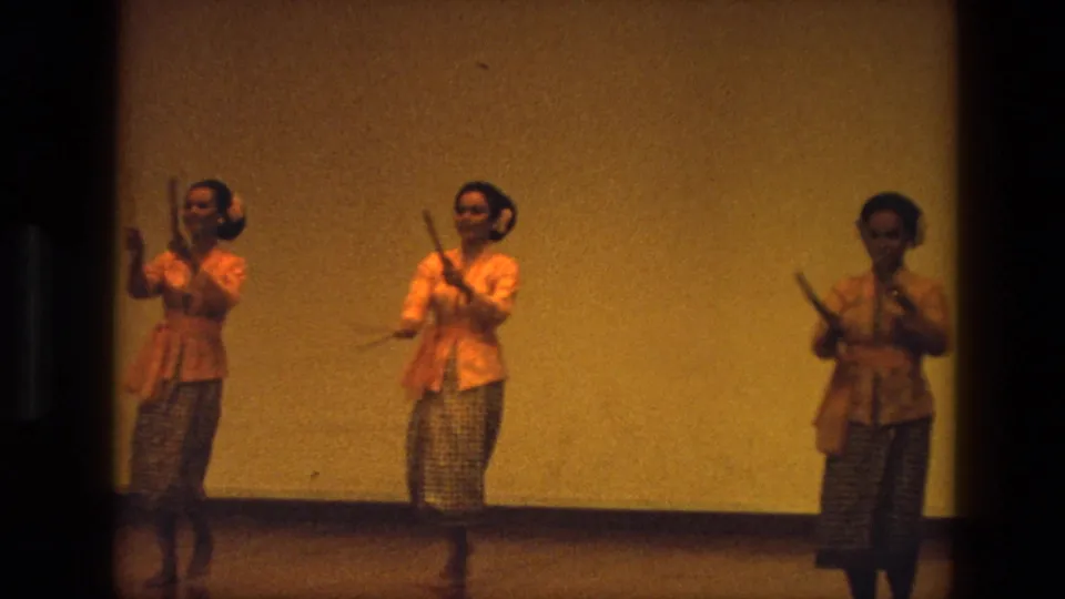 1974 India 8mm frame showing women dancers with sticks in a staged traditional performance, framed by dark film edges.