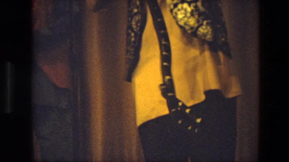 1974 India home-movie close-up of a stage performer in yellow clothing and dark decorated vest, cropped by handheld framing.