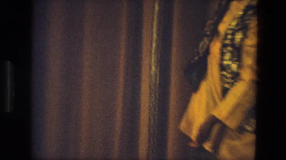 1974 India 8mm frame showing a blurred partial view of the stage performer in traditional-style clothing near the curtain.