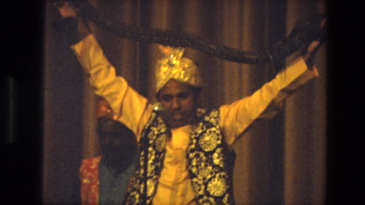 Performer in golden headwear raises a long snake in front of stage curtains.