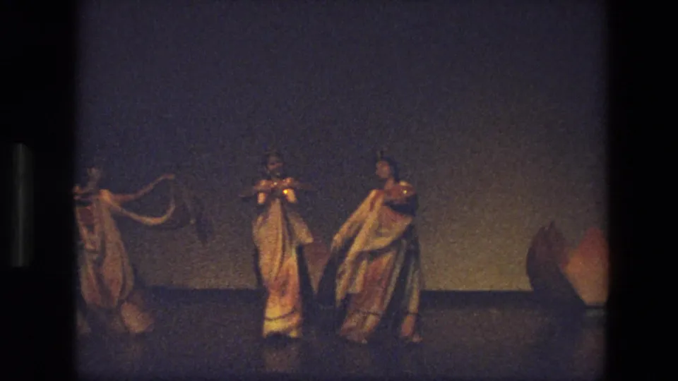 1974 India 8mm frame of dancers in flowing costumes and veils performing across a dim stage under warm light.