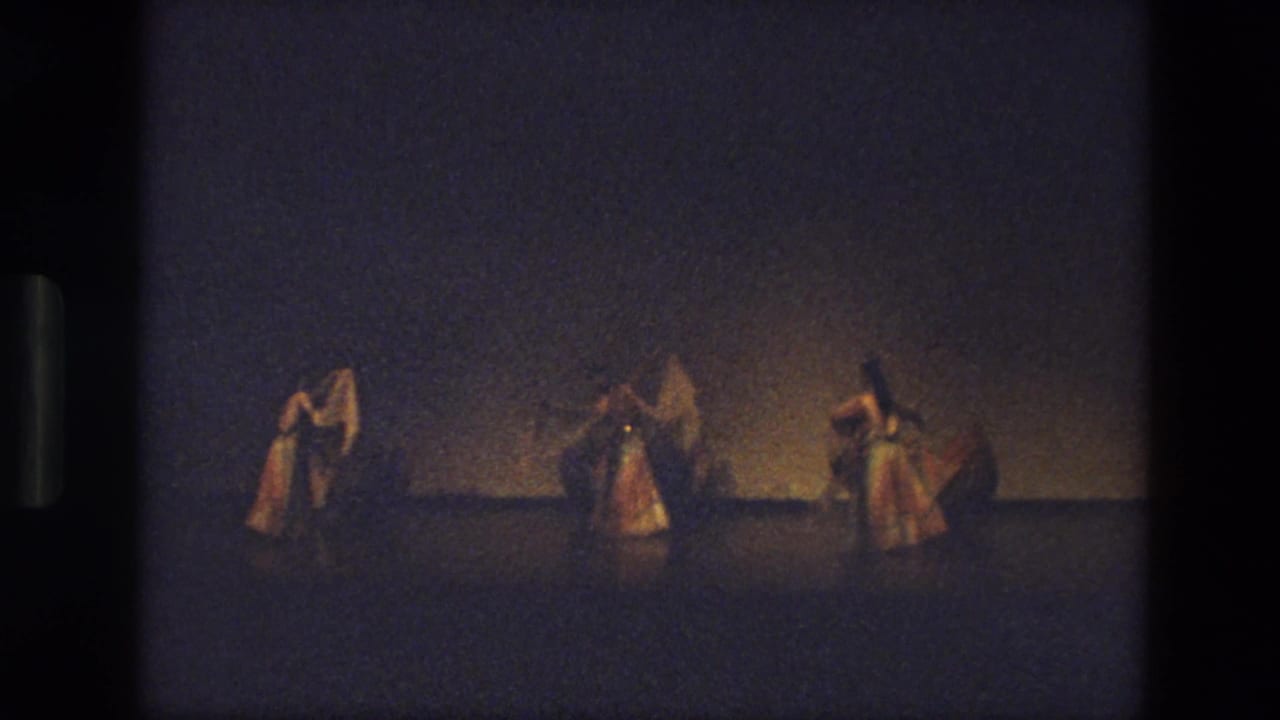 Three female dancers appear spaced across a plain stage in India, each lifting or shaping a veil under warm theatrical light.
