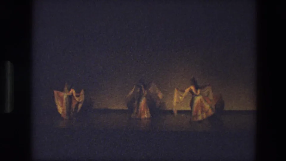 A 1974 India stage scene shows dancers in flowing costumes bending and turning with fabric veils in soft, grainy 8mm light.