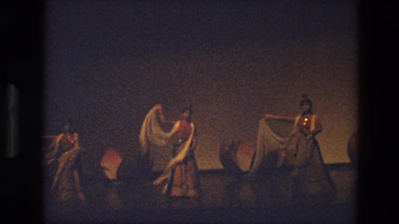 1974 India 8mm frame showing three women performing a staged dance with white scarves before pink lotus flower props.
