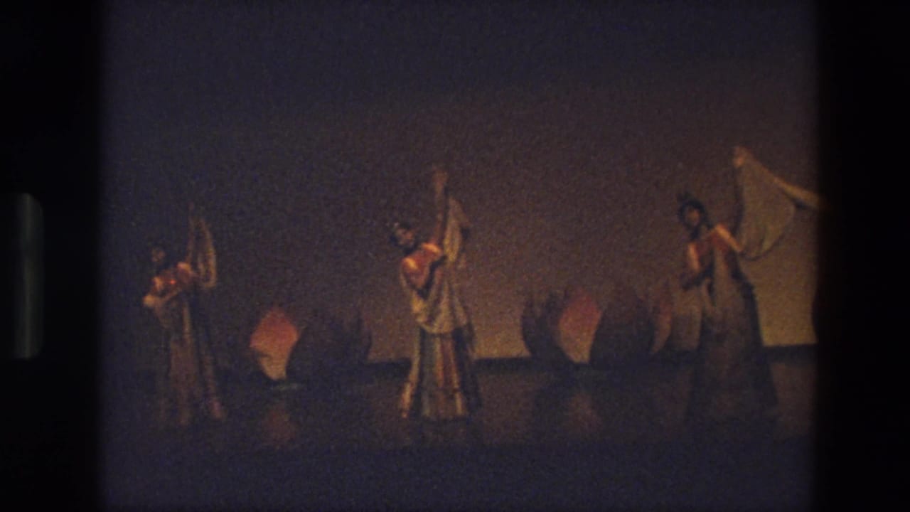 A distant 8mm view of three women in costume holding white scarves during a stage dance in India in 1974.