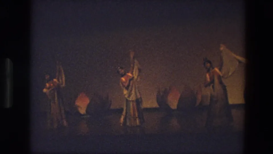 A distant 8mm view of three women in costume holding white scarves during a stage dance in India in 1974.