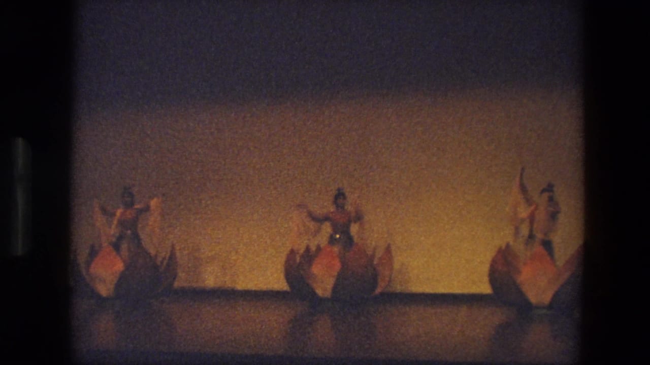 In 1974 India footage, three costumed dancers appear spaced across a stage against a plain lit backdrop.