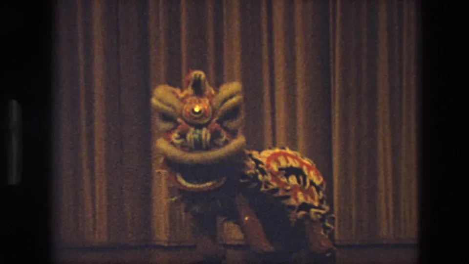 Closer 1974 India frame of a colorful lion dance costume with a bright eye in front of the stage curtain.