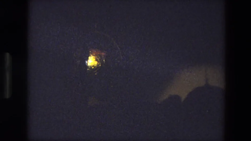 Final low-light 8mm frame from the 1974 India clip, showing a glowing point in darkness with indistinct shapes below.