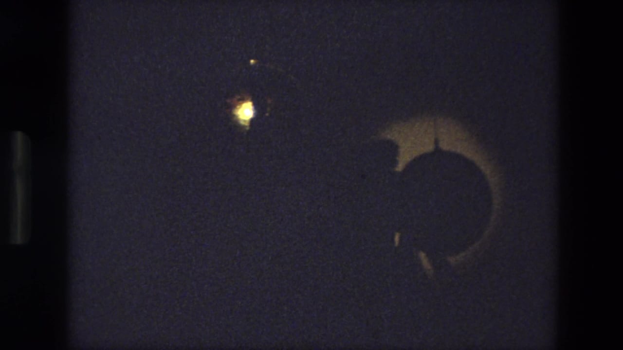 Dark stage with a crescent-shaped shadow and a small glowing light near the top.