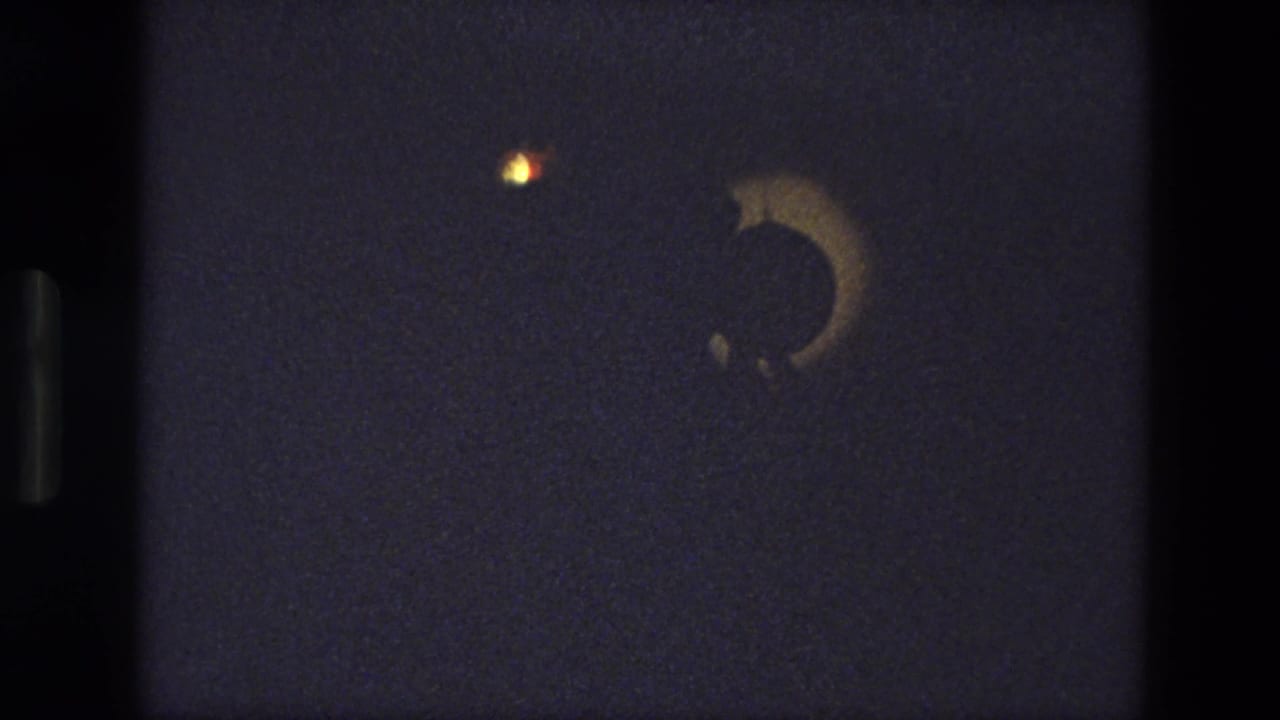 1974 India 8mm frame of a theatrical lighting effect with a crescent-shaped shadow against a dark stage.