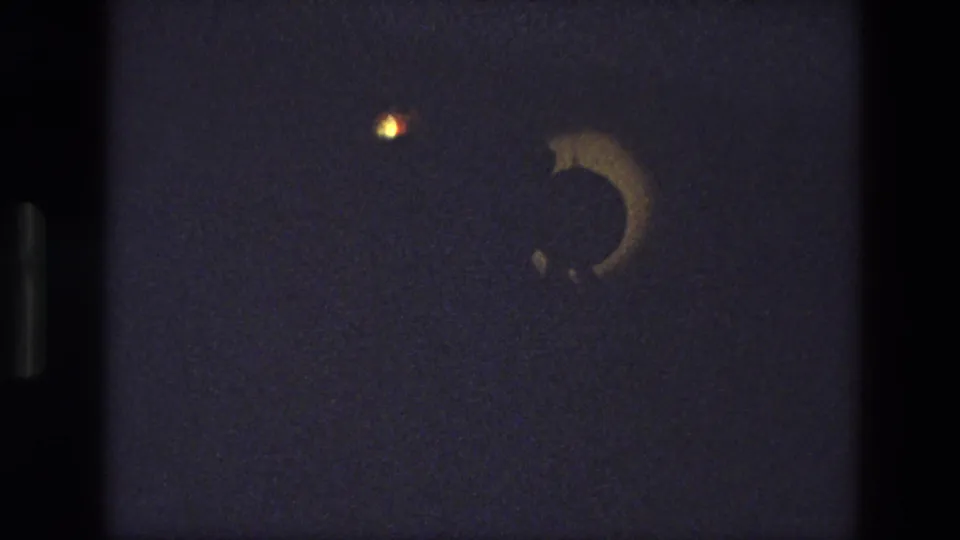 1974 India 8mm frame of a theatrical lighting effect with a crescent-shaped shadow against a dark stage.