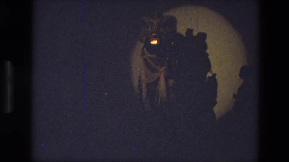 1974 India 8mm frame showing performers in theatrical costume grouped under a circular spotlight on a dark stage.