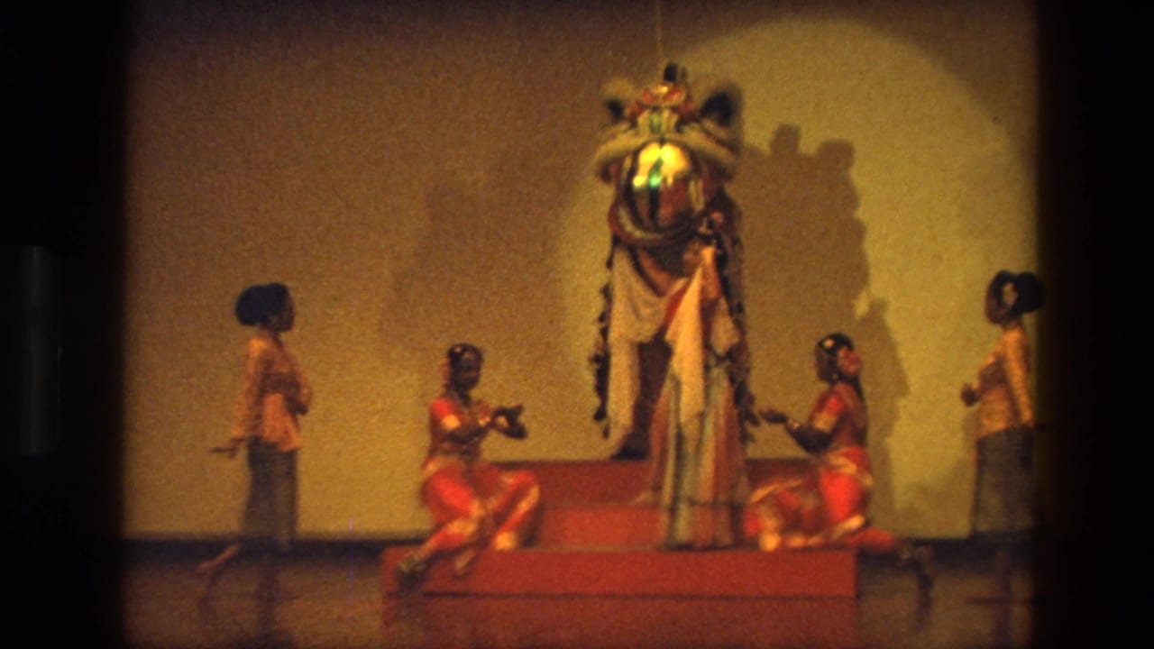 Dancers perform on a stage around a large lion costume on a raised red platform.