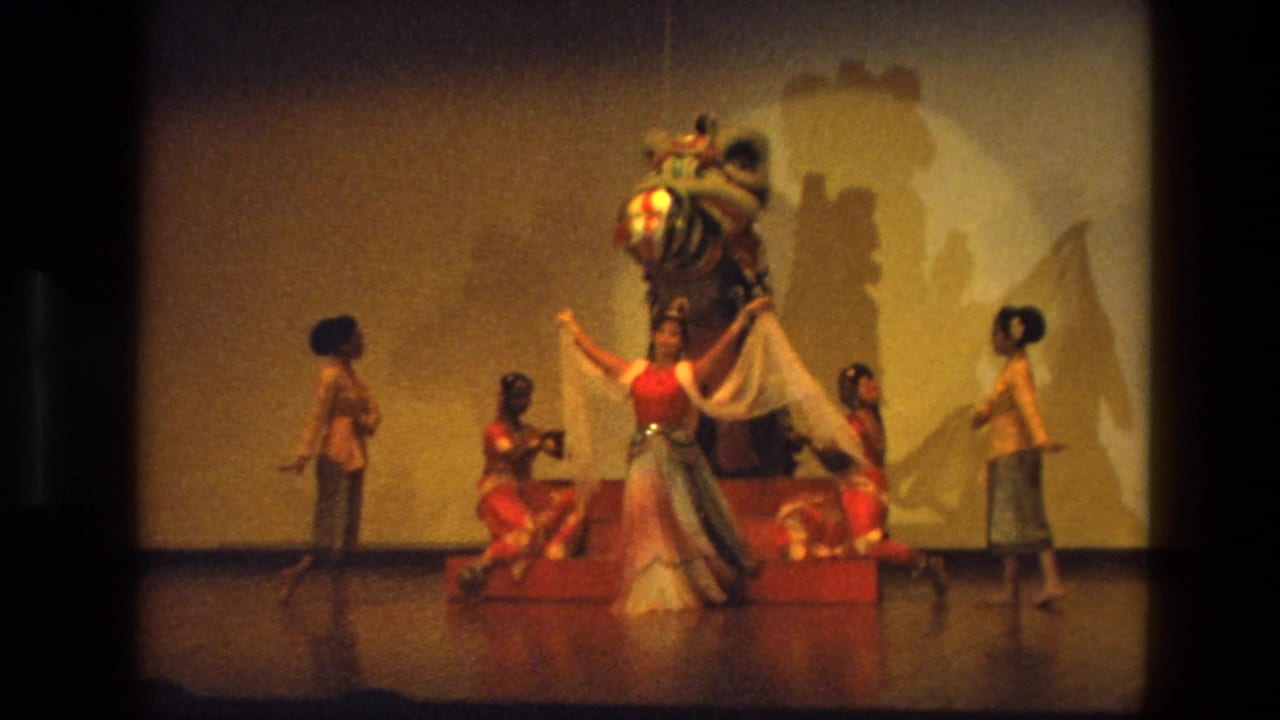 A dancer extends fabric while others kneel beside the lion costume on stage.