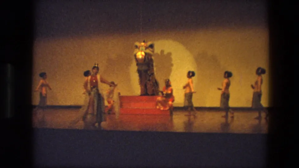 1974 India stage-performance frame with dancers and attendants arranged across the stage around a large lion-like costume.