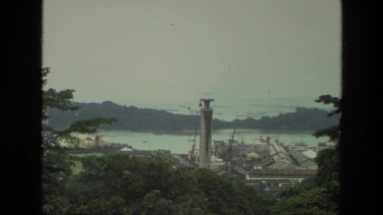 Distant dam or reservoir view with trees, water, a tall pillar structure, and dark vertical frame edges.