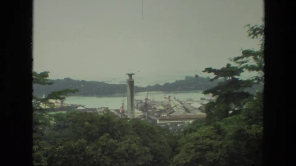 The final 1974 India frame holds a window-framed view of treetops, a waterfront town, a tall tower, and hazy water beyond.