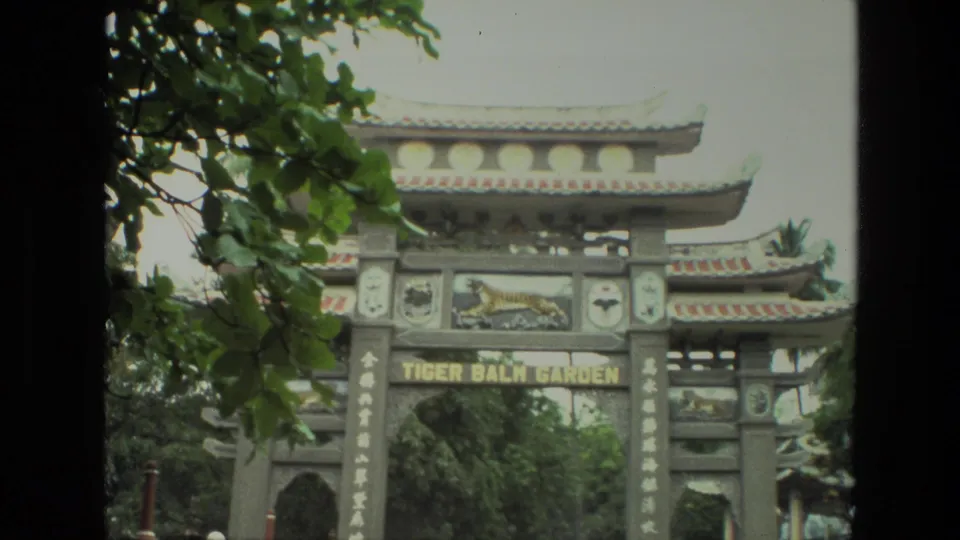 1974 India 8mm frame showing the Tiger Balm Garden entrance gate, Chinese-style rooflines, vertical lettering, trees, and a tiger relief panel.