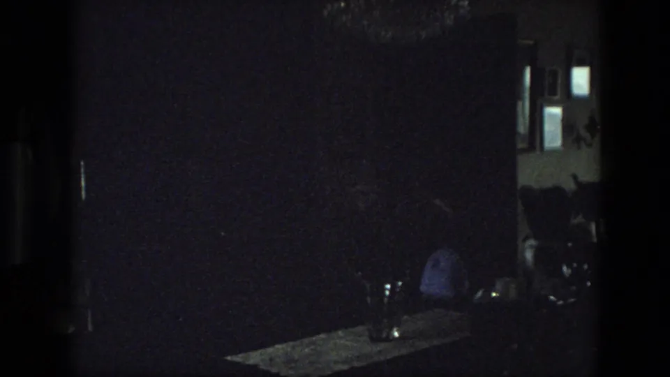 Dark 1974 India 8mm frame showing a dim interior with a bright window or doorway, a table surface, and indistinct objects.