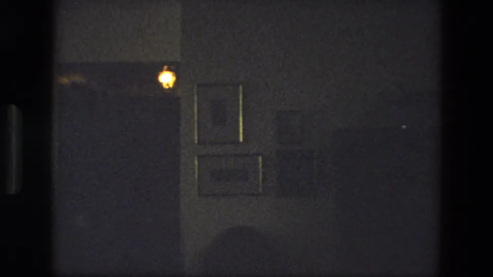 1974 India 8mm frame showing a dim private interior with framed pictures and a warm wall light near a doorway.