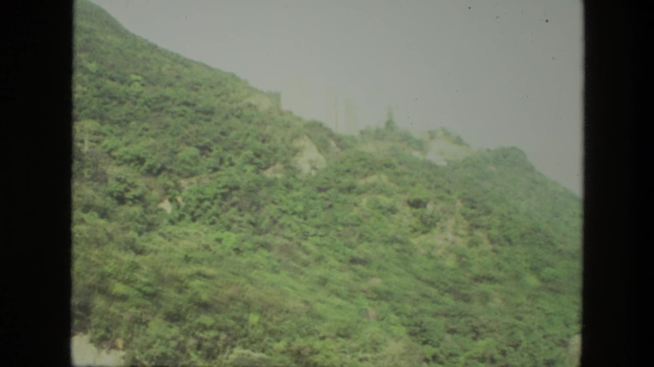 Green hillside with rocky patches beneath a pale hazy sky.