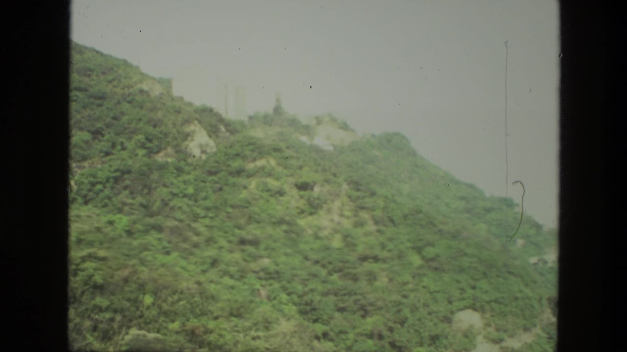 Vegetated hill ridge with rocky areas and faint structures near the top.