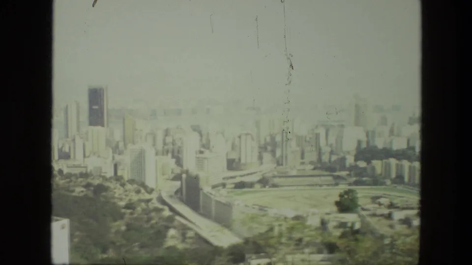 Final 1974 India pan frame with a broad urban view, roadways, high-rises, and an open green park or field area.