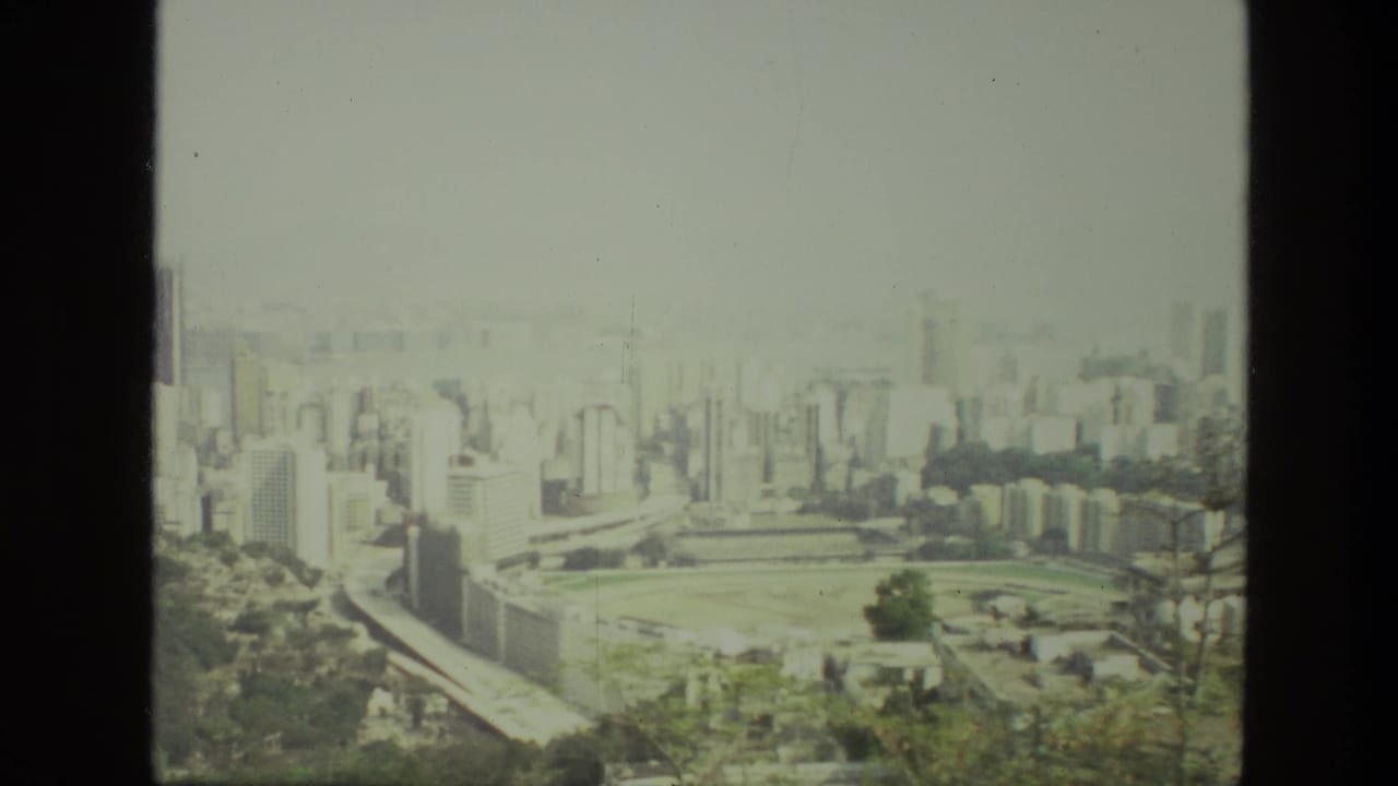 1974 India 8mm frame showing a hazy urban skyline, dense buildings, green open ground, and trees from a high vantage point.