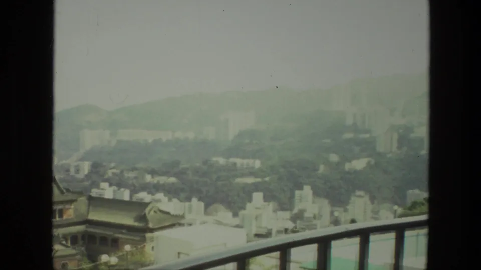 This 1974 India frame shifts lower across the hazy skyline, keeping a tiled-roof building, white blocks, hills, and towers visible.