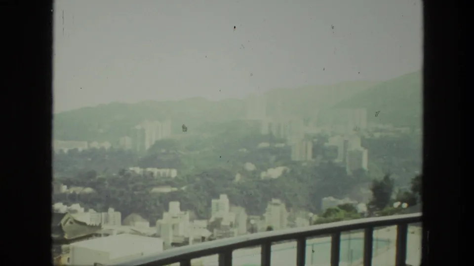 The final 1974 8mm frame shows a hazy Indian city skyline over green hills, with high-rises beyond foreground railings.