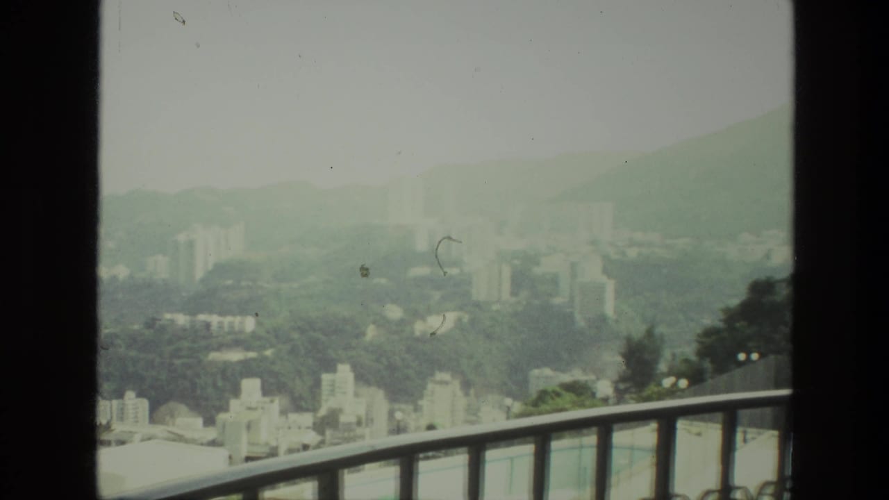 Hazy city valley seen past a balcony railing and dark window edge.