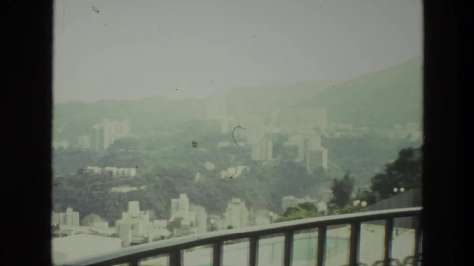 1974 India 8mm frame looking from a balcony toward a hazy hillside city with distant high-rises.