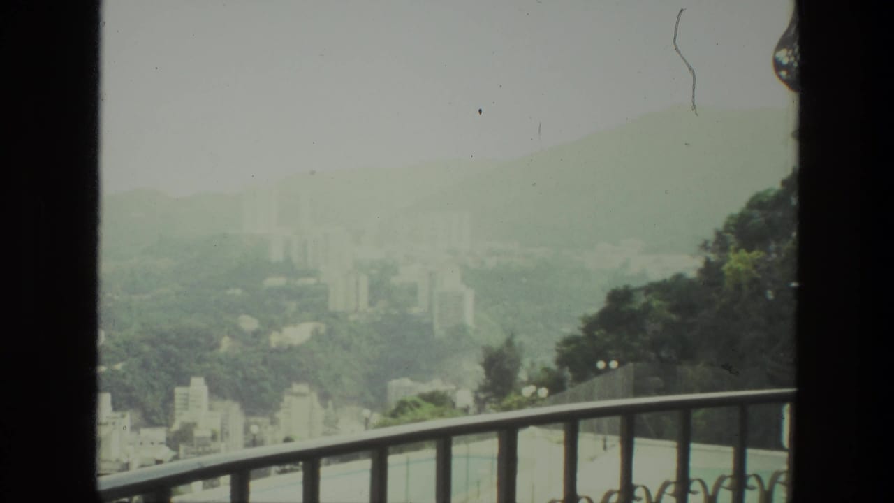 Distant buildings and green hills viewed over a balcony railing.