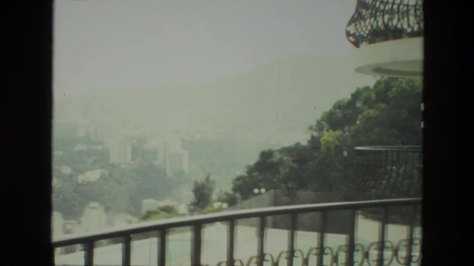 1974 India home-movie still of a hazy valley city viewed from a balcony near another building facade.