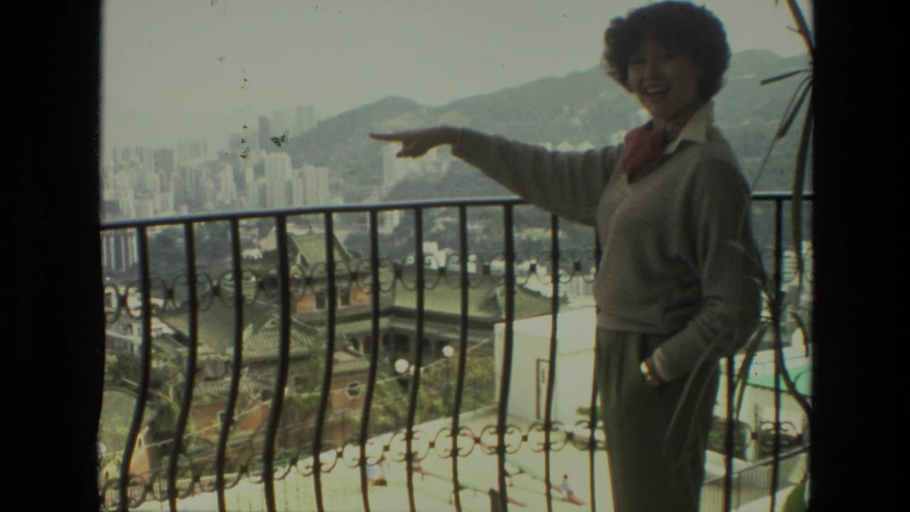 Woman smiling and pointing from a balcony toward the distant city view.